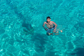 Youngman looking at to camera in beautiful turquoise color, transparent sea.