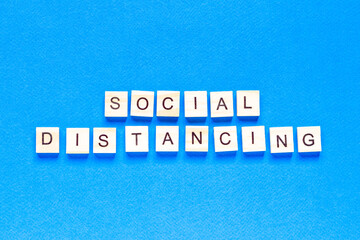 Words social distancing. Wooden inscription on a blue background. Information sign of social distancing from blocks on a blue background.