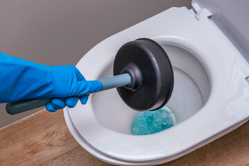 A clean toilet with cleaning agent and a gloved hand with a plunger. The concept of the home...