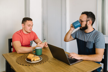 Two men sitting using laptop and phone.