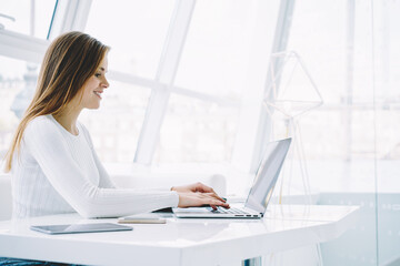 Smiling copywriter typing text information on keyboard of computer sitting in stylish...