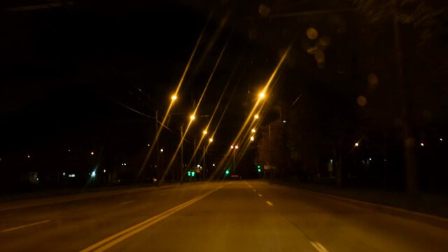 4k. night drive on empty city street road from the window of speed car, steet light blurring after rain.