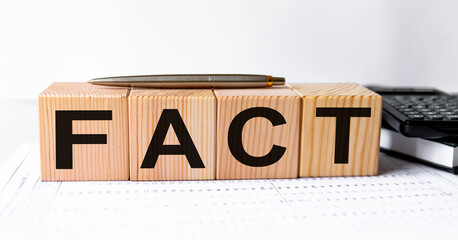 Wooden blocks with letters forming concept word 'fact' on wooden cubes with pen on a beautiful financial background.