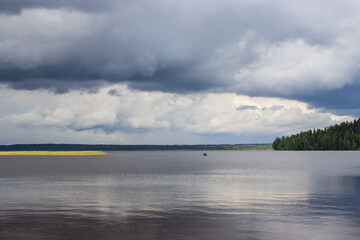 Fototapeta premium Landscape with a boat sailing on the lake. There are dramatic clouds in the sky.