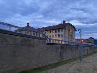 Fototapeta na wymiar Gefängnisgebäude hinter dicken Mauer mit Stacheldraht zur Abend-Stunde