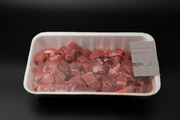 Raw diced meat (chopped in cubes) in a white styrofoam container with barcode on it isolated on black background with copy space for text