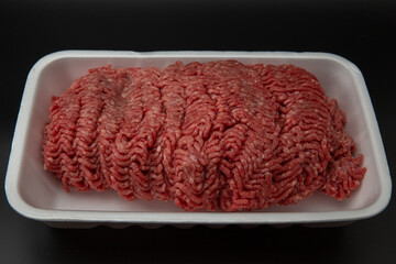 Raw minced (ground) meat in a white styrofoam box isolated on black background with copy space for text