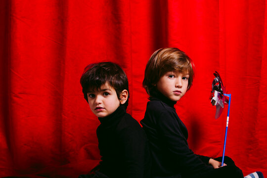 Two boys wearing black clothes against a red curtain