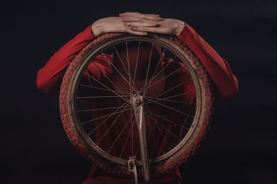 
A concentrated rider covered by a cap tilts his head on the front wheel of his injured bicycle.