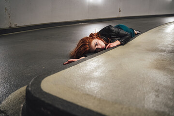 Red haired female model laying on floor inside parking house along curb. Young woman with open eyes...