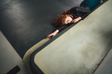 Top view of red haired girl laying on floor inside parking house along curb. Young woman with...