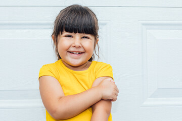 Adorable little girl with black hair wearing a yellow shirt leaning against white background