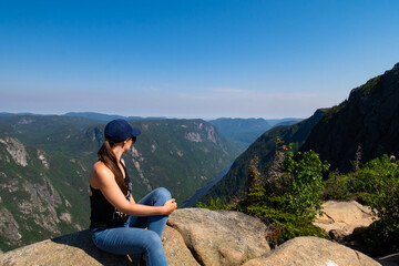 Naklejka premium Young woman standing on the edge of a cliff at the summit of a mountain in the Hautes-gorges-de-la-rivière-Malbaie national park, Canada 