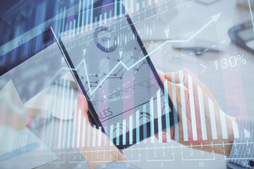 Double exposure of man's hands holding and using a phone and financial graph drawing. Analysis concept.