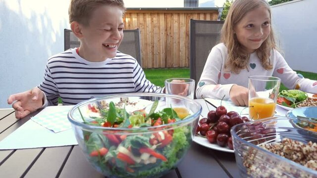 Two Appy Teen Children Eating With Parents Healthy Dinner On Terrace At Back Garden