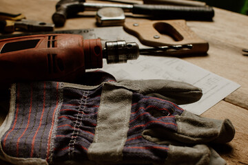 Tools for construction and carpentry: industrial gloves, drill, hammer and meter on wooden table. home repair concept.