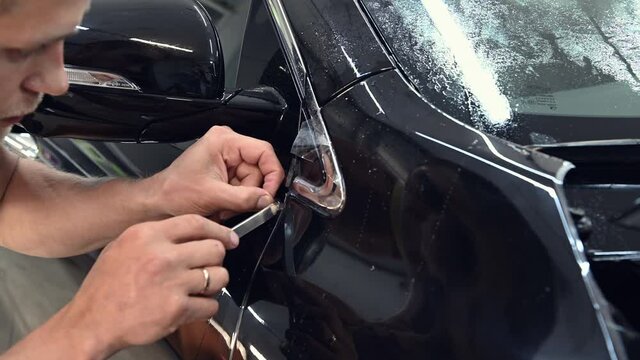 Close up of applying a protective film on the car. Hand of a professional cut with a knife edges of protection film