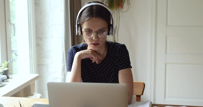 Student sit at table use headphones wear eyeglasses talk with tutor by online videocall conference app. English language practice discuss common project with schoolmate distantly work together concept