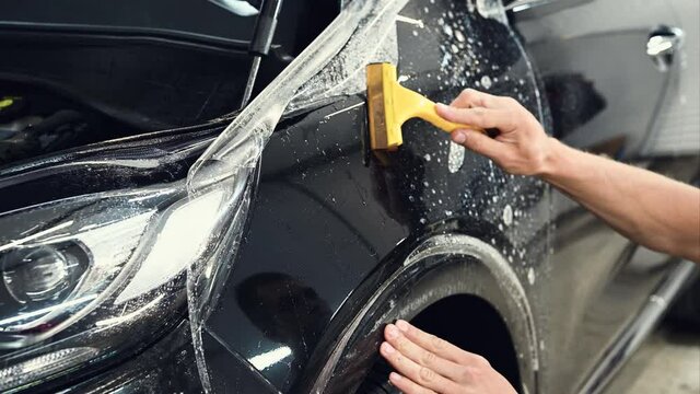 Close up shot of the hands of man who unstick the film with black cowl of a car. This film protects the vehicle from the damage.