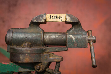 Vice grip tool squeezing a plank with the word lackey - obrazy, fototapety, plakaty