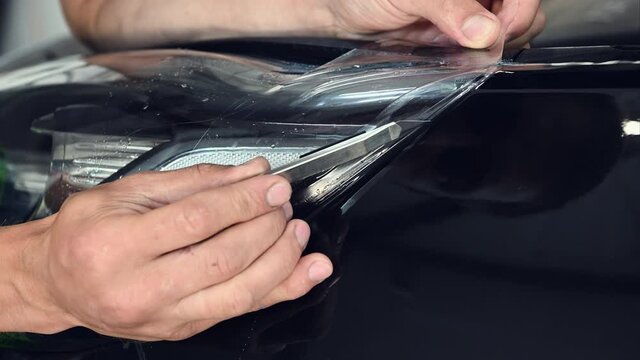 Close up shot of master cutting vinyl film by special knife. Expert makes neat cut for further bonding film on the car surface.