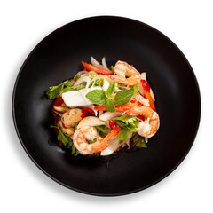 Spicy vermicelli salad with seafood served on black plate on white background, Thai cuisine.