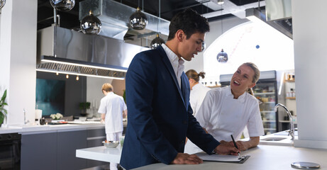 Manager and female chef discussing over a clipboard at restaurant kitchen