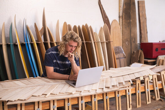 Man using laptop in the surfboard studio - Powered by Adobe