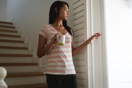 Woman with coffee cup looking out of window at home