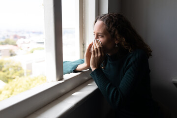 Woman blowing her nose near the window at home