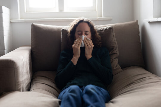 Woman blowing her nose on the couch at home