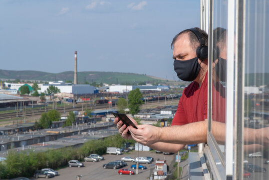 reading news about coronavirus. man listens to the news in headphones on the balcony of the house. man in a protective medical mask. selective focus. continuous wearing of the surgical protective mask
