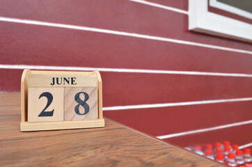 June 28, Number cube with wooden table beside the wall.