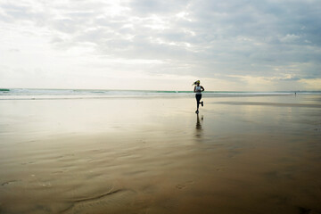 wide lens silhouette of African American runner woman jogging on the beach - young attractive and athletic black girl training outdoors doing running workout at the sea