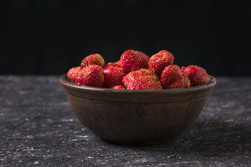 Ripe strawberries in a clay bowl on the table on a black background.