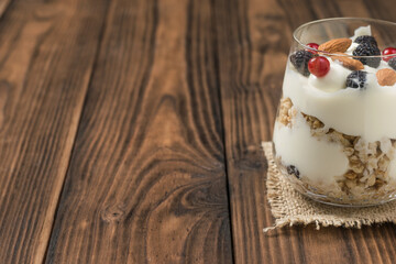 A glass of granola, yogurt, berries and almonds on a brown wooden table.