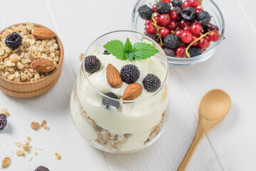 Yogurt with granola, blackberries and almonds in a glass glass on a white table.