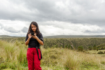 Woman checking her cell phone on a landscape with a camera on her arm