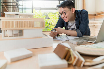 young attractive asian glasses male architect smile confident proud to present new project house model ,happiness asian working with mass model study of house design project