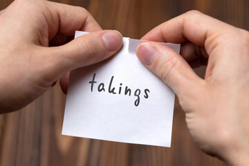Hands of a man tearing a piece of paper with inscription takings
