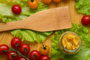Pasta with vegetables in a plate. Ingredients for cooking tomatoes, cherry greens.  With basil. Background from spaghetti. On the table, top view. 