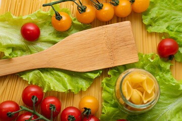 Pasta with vegetables in a plate. Ingredients for cooking tomatoes, cherry greens.  With basil. Background from spaghetti. On the table, top view. 