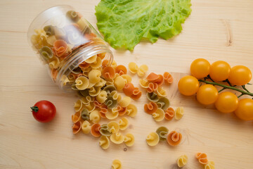 Macaroni is scattered on the table. Ingredients for the preparation of Italian pasta tomatoes, cherry greens. Background from spaghetti.