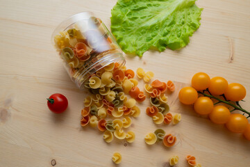 Macaroni is scattered on the table. Ingredients for the preparation of Italian pasta tomatoes, cherry greens. Background from spaghetti.