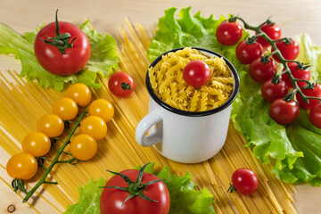 Pasta with vegetables in a plate. Ingredients for cooking tomatoes, cherry greens. Background from spaghetti. White enameled mug.