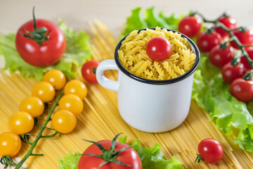Pasta with vegetables in a plate. Ingredients for cooking tomatoes, cherry greens. Background from spaghetti. White enameled mug.