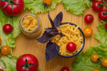 Pasta with vegetables in a plate. Ingredients for cooking tomatoes, cherry greens.  With basil. Background from spaghetti. On the table, top view. 