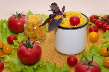 Pasta with vegetables in a plate. Ingredients for cooking tomatoes, cherry greens. Background from spaghetti. White enameled mug.
