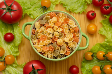 Pasta with vegetables in a plate. Ingredients for cooking tomatoes, cherry greens.  With basil. Background from spaghetti. On the table, top view. 