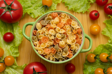 Pasta with vegetables in a plate. Ingredients for cooking tomatoes, cherry greens.  With basil. Background from spaghetti. On the table, top view. 